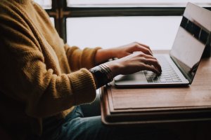 Woman in mustard sweater typing on laptop
